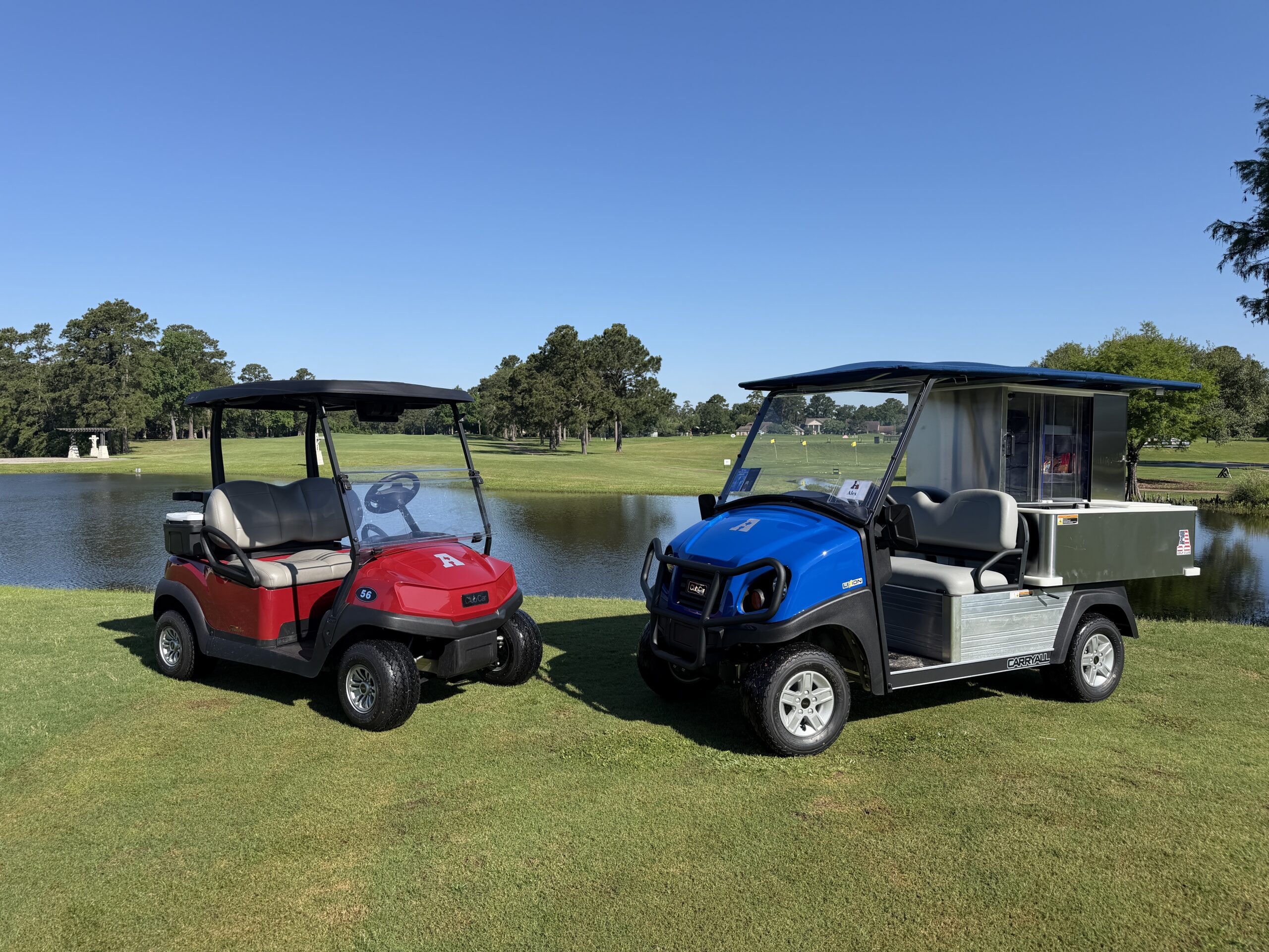 Red golf cart and blue beverage/snack cart in the sun by the lake.